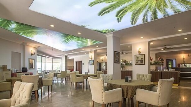 A spacious hotel lobby with a high ceiling, palm leaf ceiling design, and a central round dining table surrounded by chairs. - Mysea Hotels Incekum (Alanya)