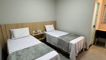 Quarto de hotel com duas camas de solteiro, cabeceira de madeira, mesa de cabeceira com telefone e pequena escrivaninha com cadeira.