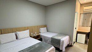 A hotel room with two beds, a nightstand, a desk, and a refrigerator.