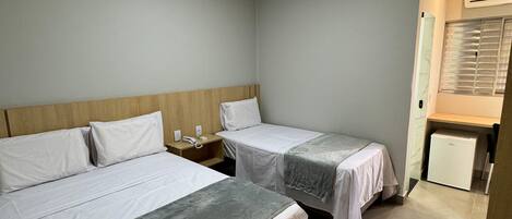 A hotel room with two beds, a nightstand, a desk, and a refrigerator.