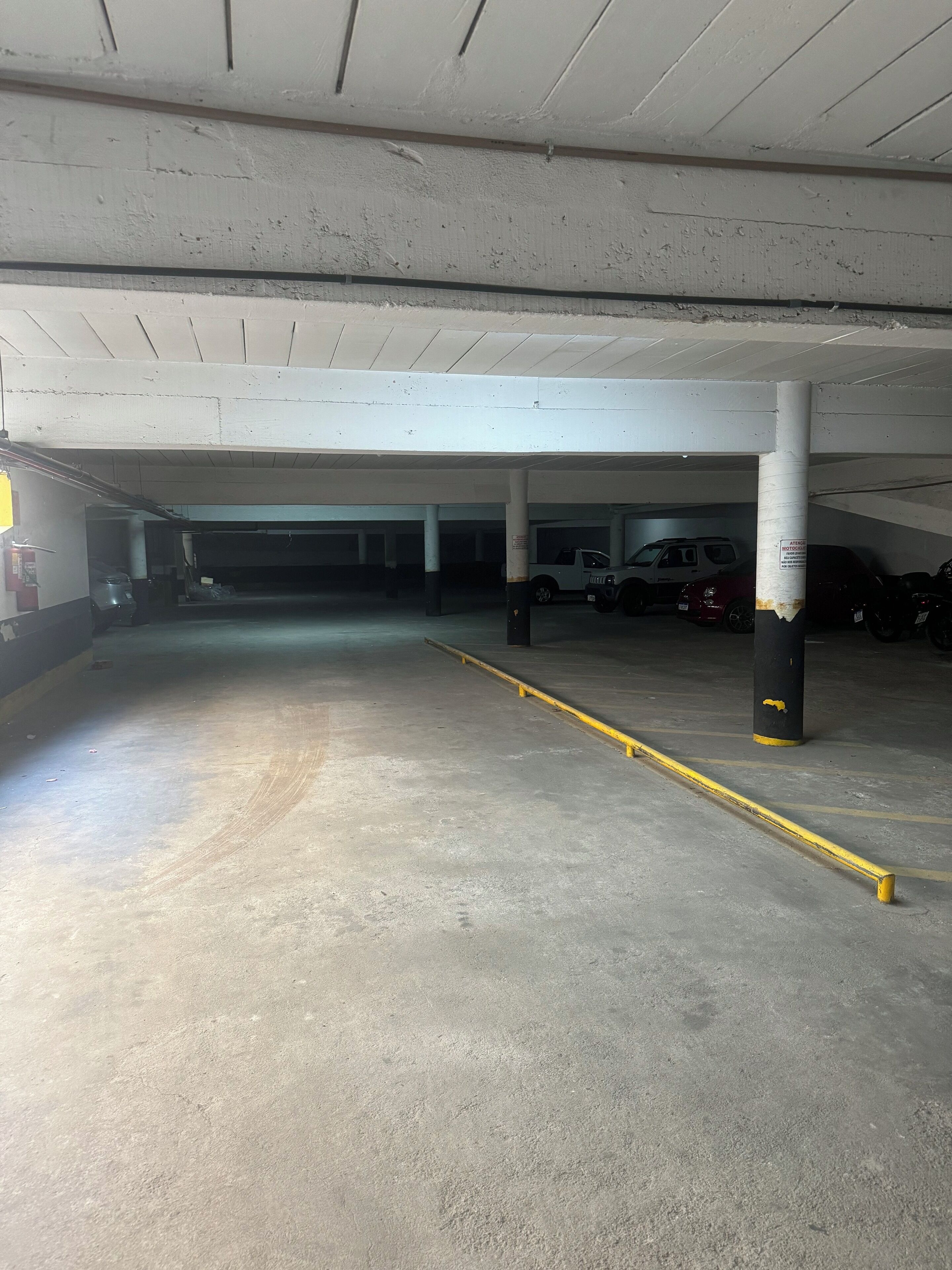 A parking garage with concrete floors and white ceilings, featuring several parked vehicles and a yellow safety line.