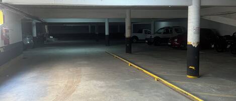 A parking garage with concrete floors and white ceilings, featuring several parked vehicles and a yellow safety line.