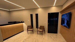 A modern lobby with a reception desk, two chairs, a television, and a marble floor.