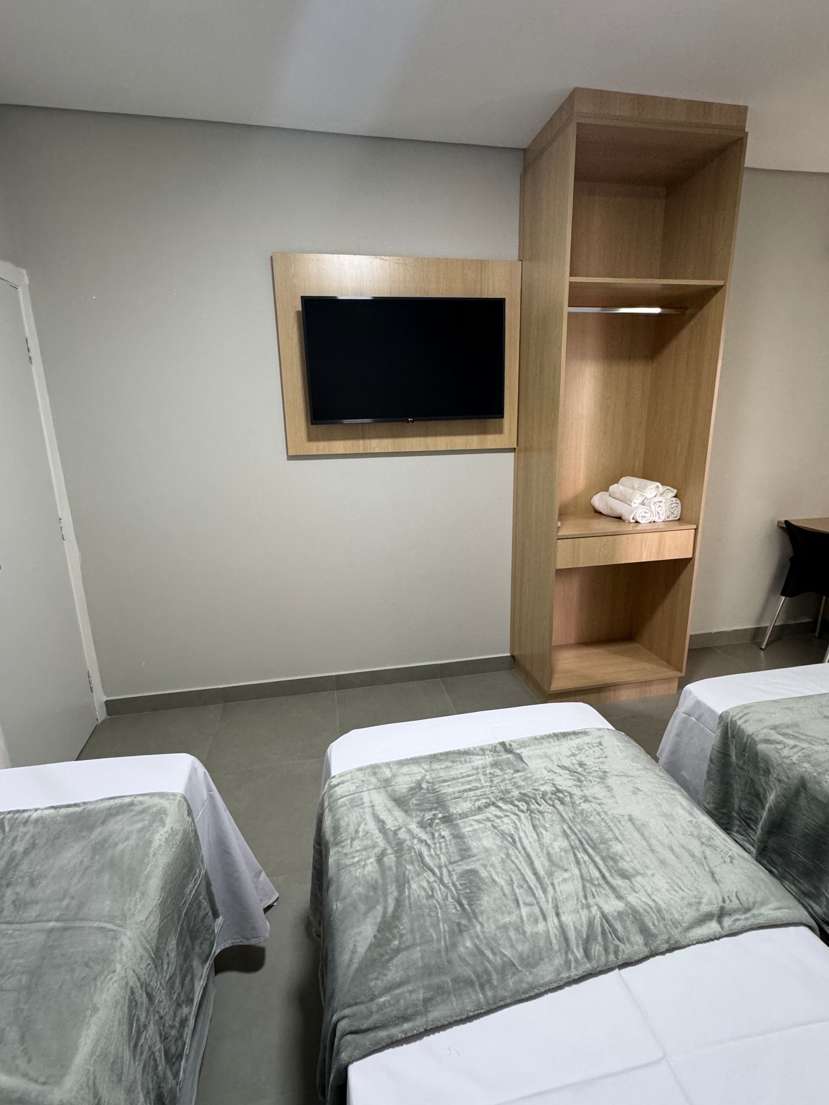 Habitación de hotel con dos camas, un televisor instalado en la pared y un armario de madera.