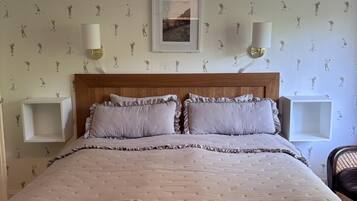 Une chambre à coucher avec un lit, deux tables de chevet, une lampe suspendue et un tableau encadré au mur.