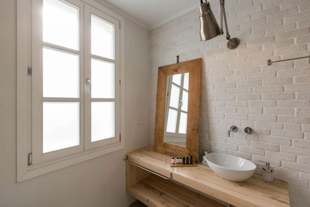A bathroom with a white brick wall, a wooden vanity, a large mirror, and a white vessel sink.