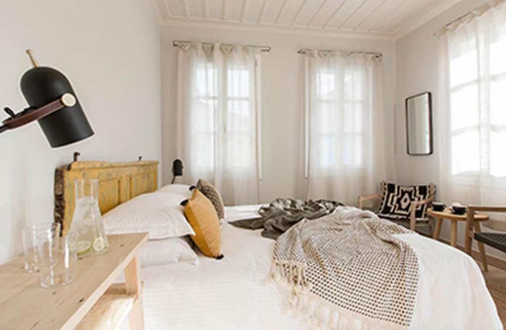 Une chambre à coucher avec une tête de lit en bois, un lit avec une literie blanche et grise, une petite table avec des verres et une chaise.