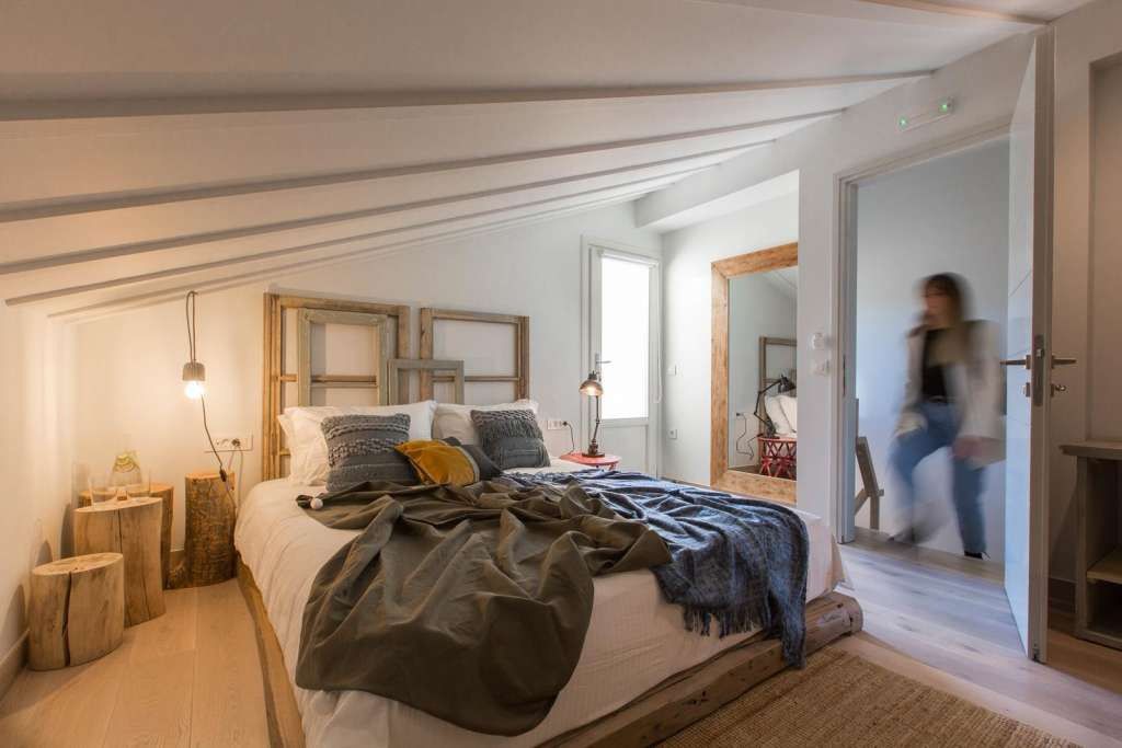A bedroom with a large bed, wooden beams, and a view of a hallway.