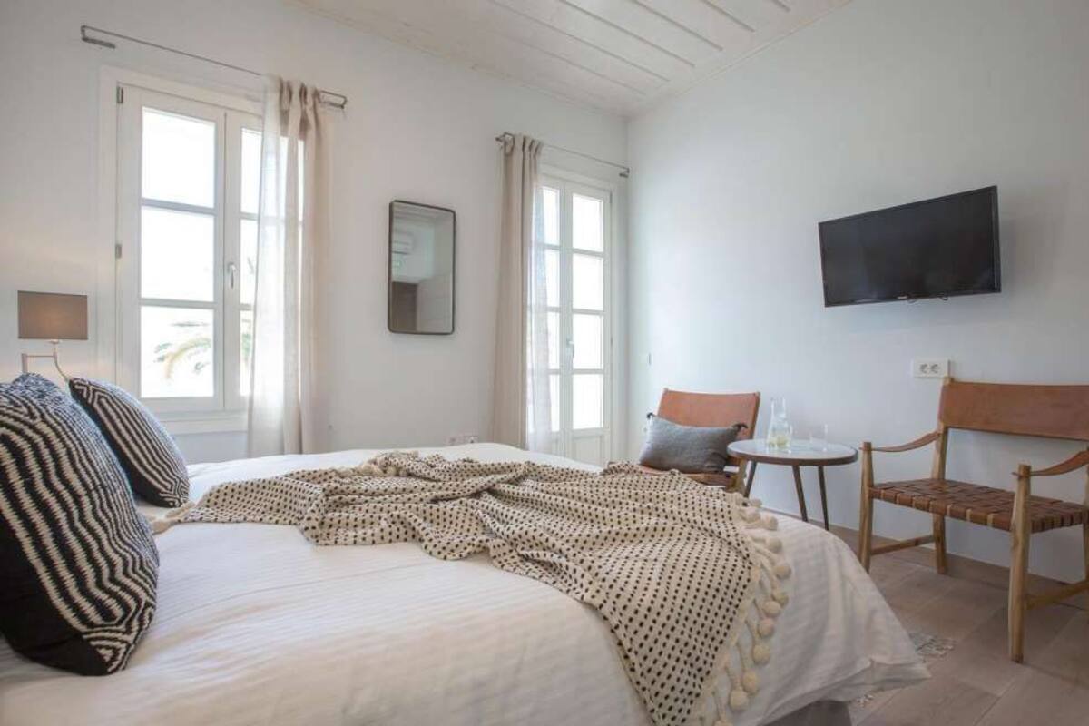 Une chambre à coucher avec un lit, une télévision, une chaise, une petite table et une fenêtre avec des rideaux.