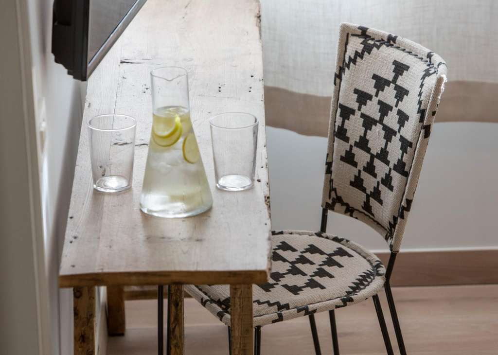 A wooden table with two glasses and a pitcher of lemonade, a patterned chair, and a television on the wall.