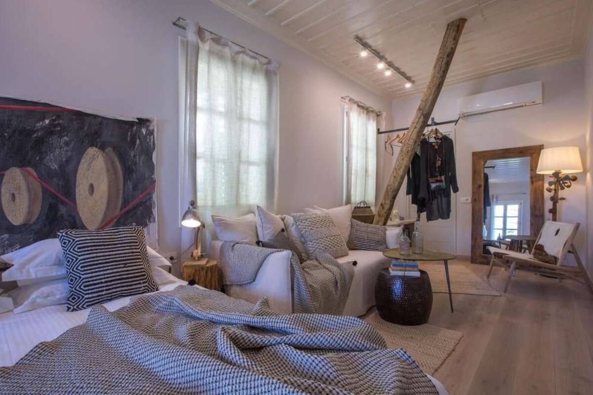 Une chambre à coucher avec un grand lit, une table de chevet, une chaise, un porte-manteau suspendu et une fenêtre avec des rideaux.
