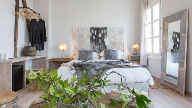 A bedroom with a bed, bedside tables, a mirror, and a hanging rack with clothes. - Amymone Suites (Nafplio)