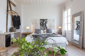 Un dormitorio con cama, mesitas de noche, un espejo y un perchero con ropa.