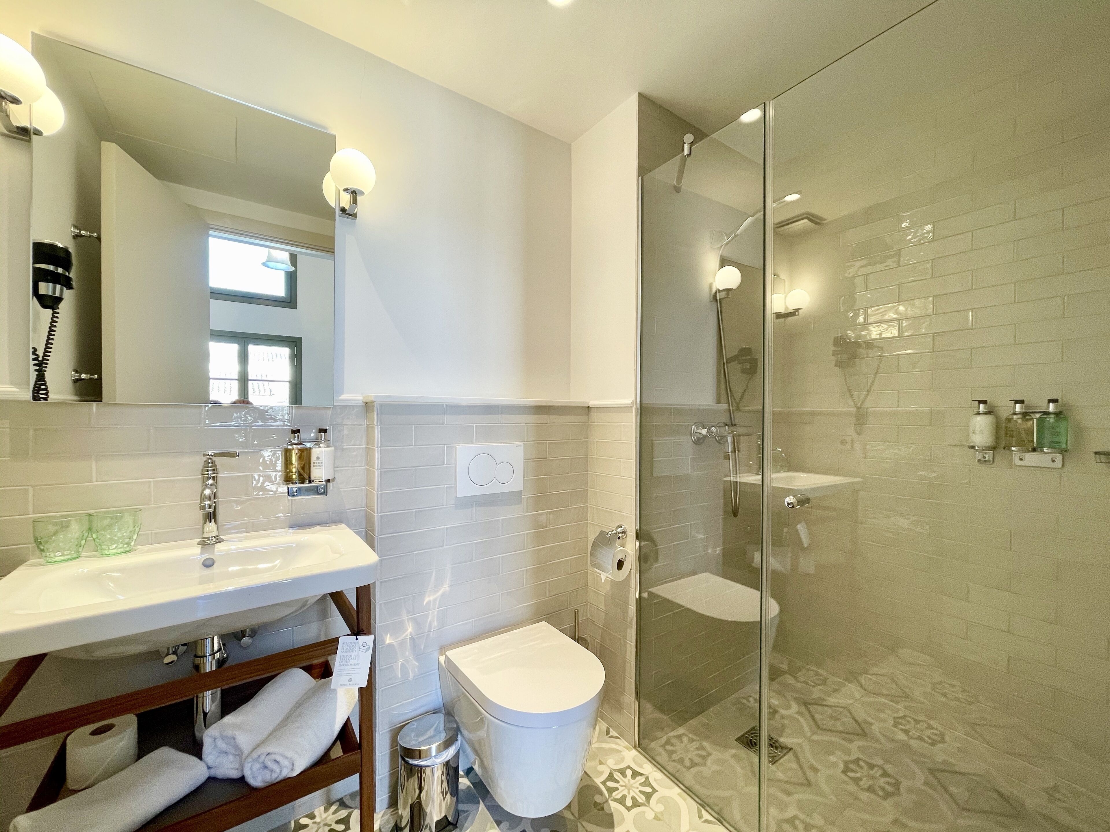 Un baño moderno con ducha de vidrio, lavamanos blanco y espejo sobre el mueble.