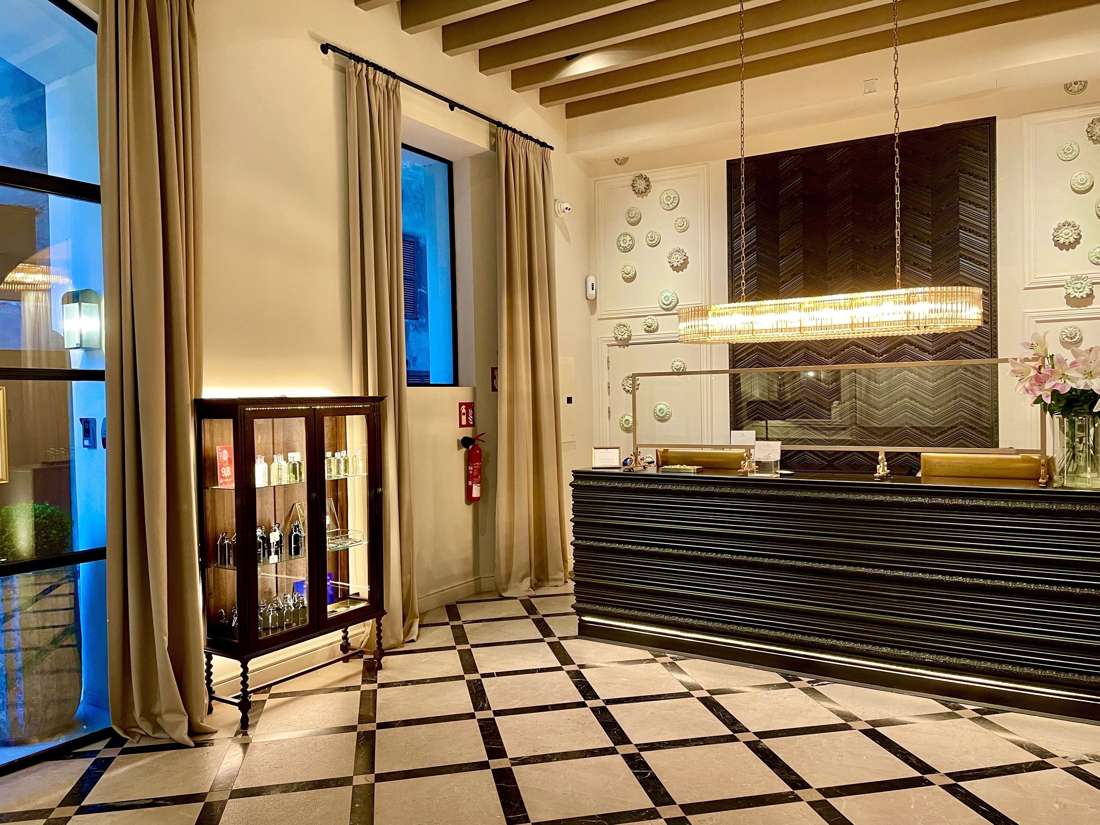 A hotel lobby with a checkered floor, a reception desk, a large mirror, and a fire extinguisher.