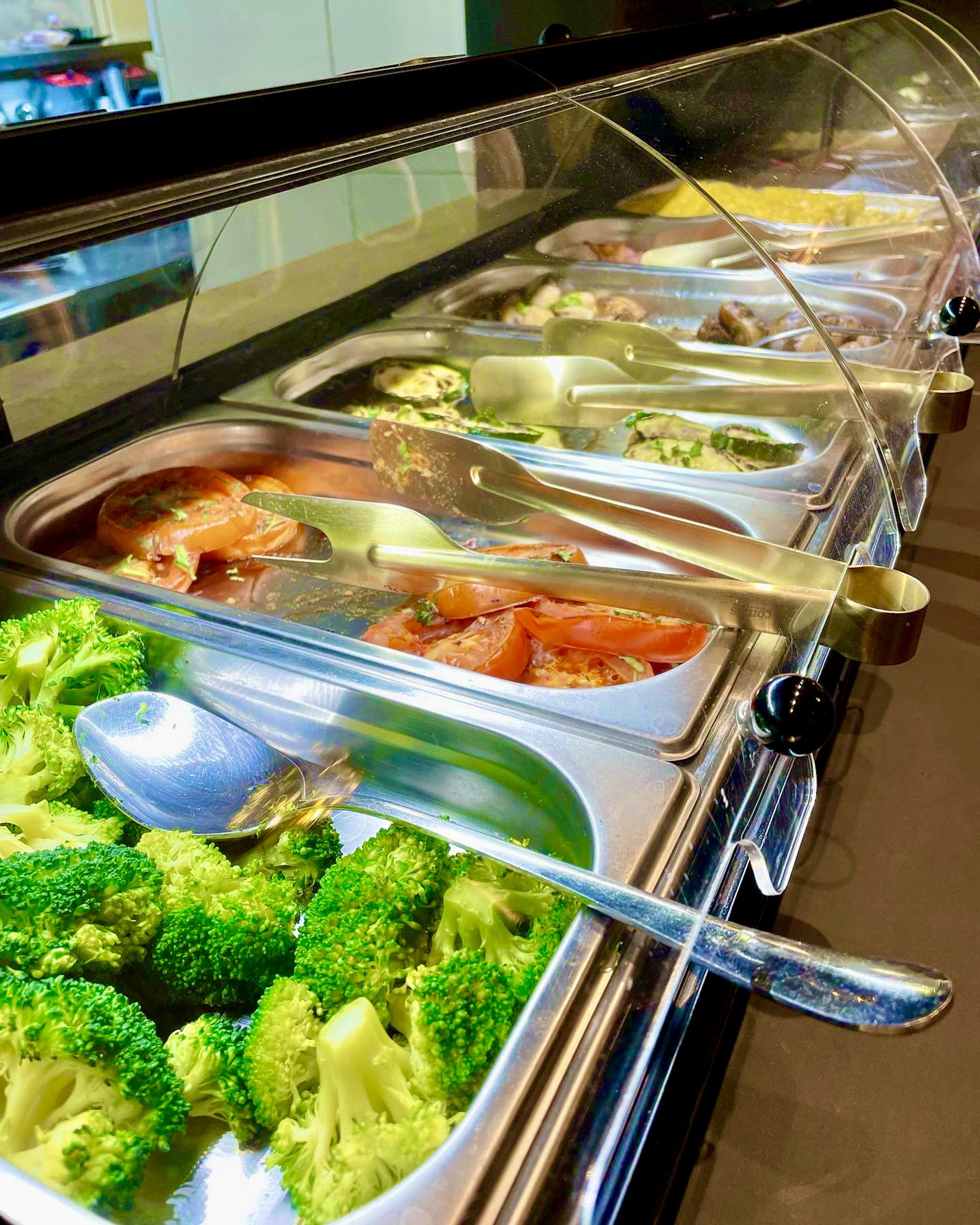 A buffet with various food options including broccoli, tomatoes, and other vegetables.