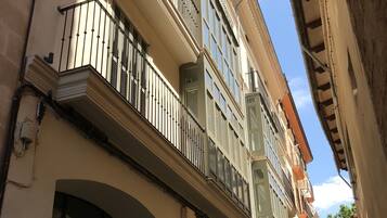 A narrow street with multi-story buildings, balconies, and a clear sky.