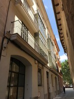 Una calle estrecha flanqueada por edificios de varios pisos, balcones y un cielo despejado.
