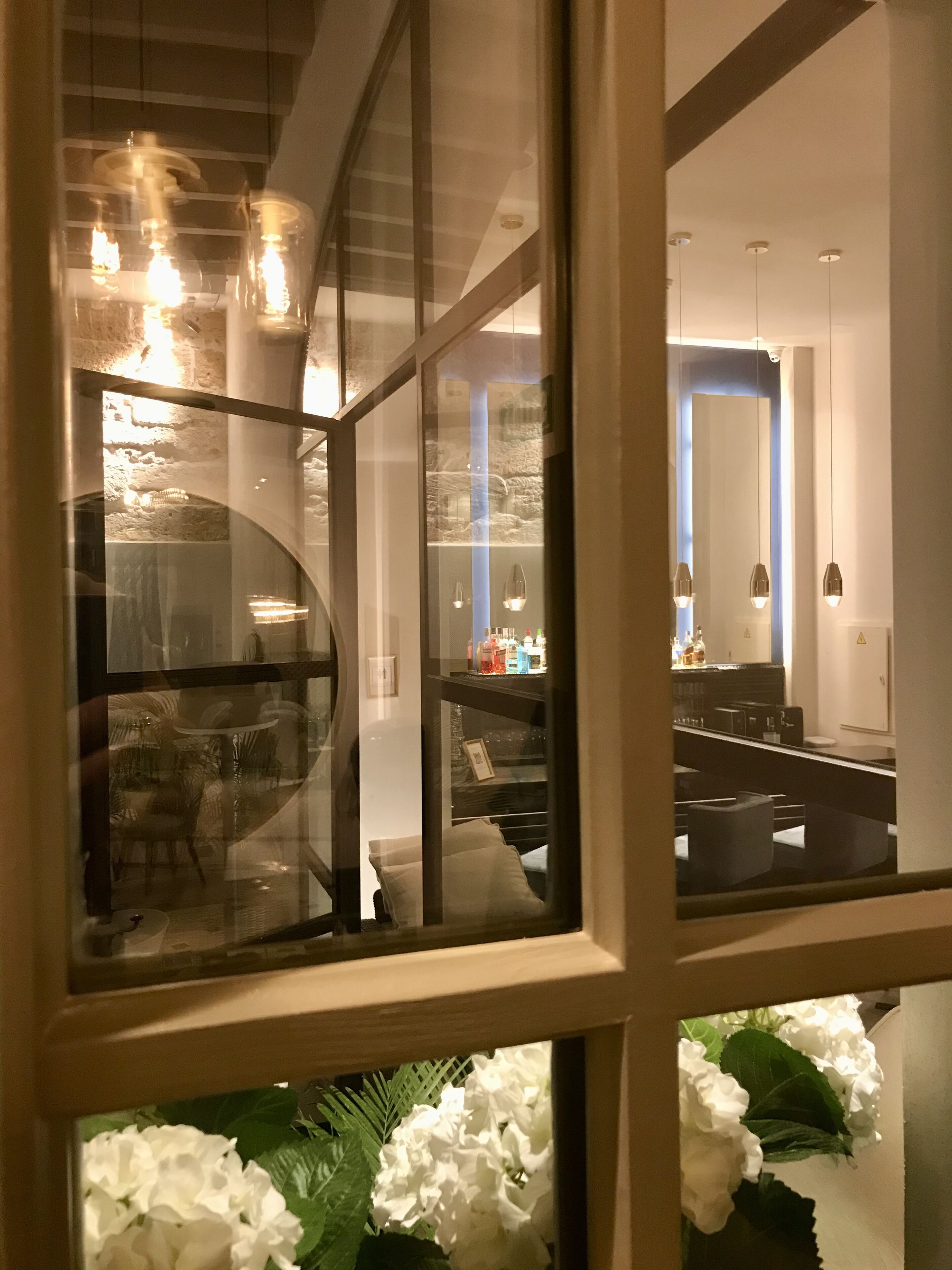 Un interior moderno con un separador de vidrio, una zona de comedor con sillas, una barra con mostrador y un espejo grande que refleja el espacio.