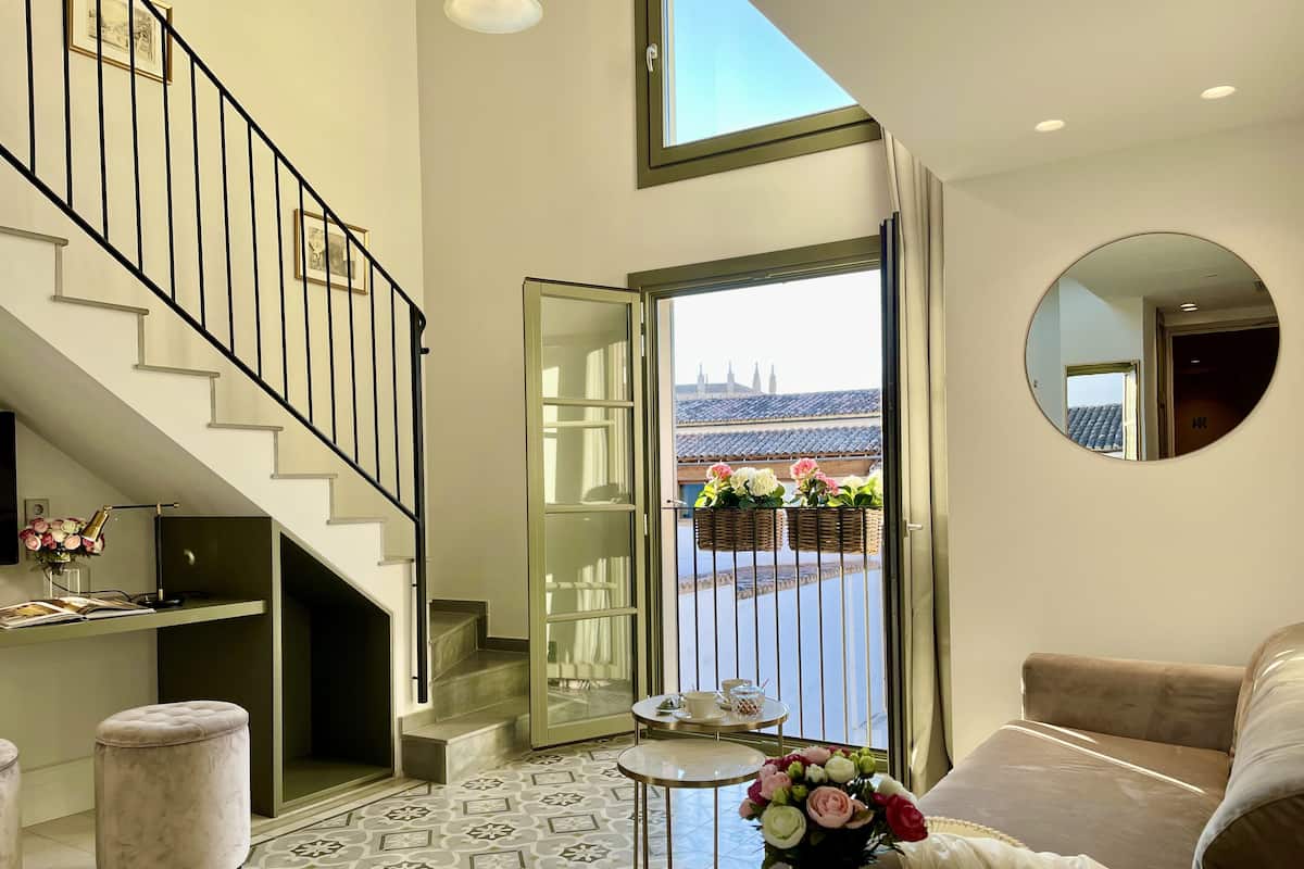 A spacious living area with a staircase, a balcony with a view, and a round mirror on the wall.