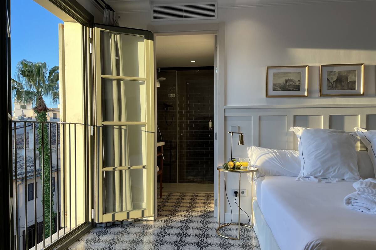 A hotel room with a bed, a small table with a lamp, and a view of the outside balcony.