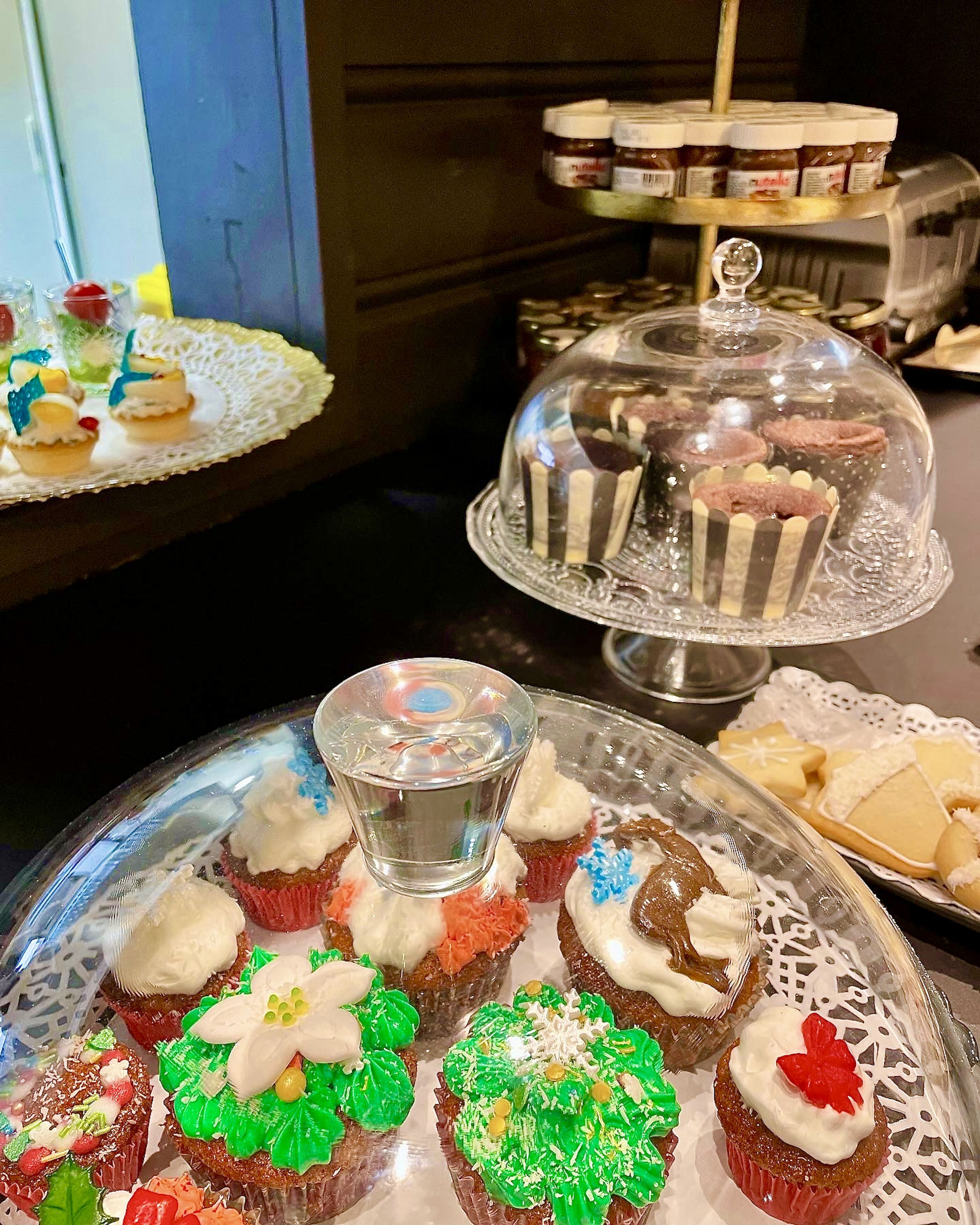A dessert display with various cupcakes and pastries, including a glass dome cover.