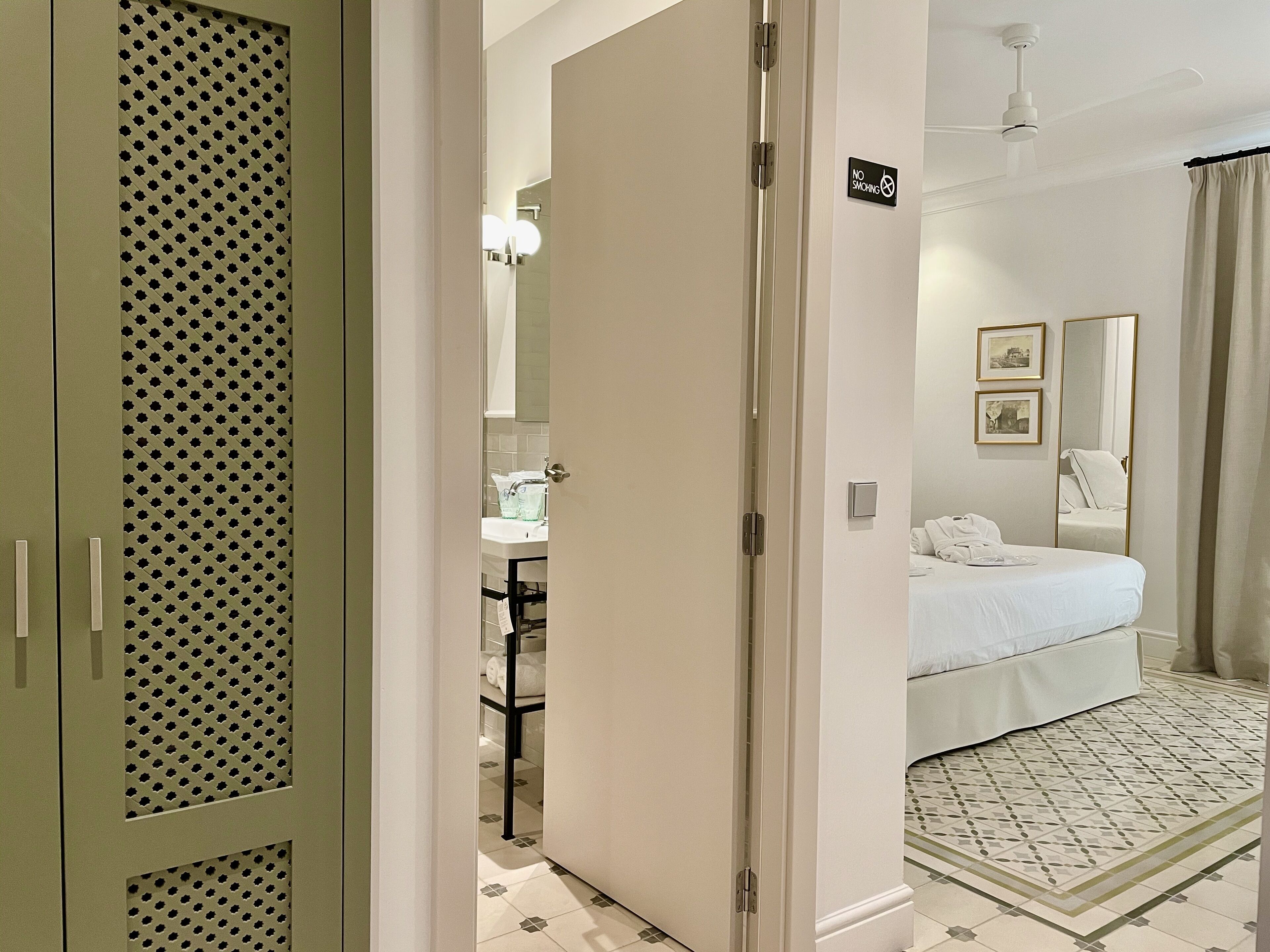 A hotel room with a bed, a bathroom with a sink, and a mirror.
