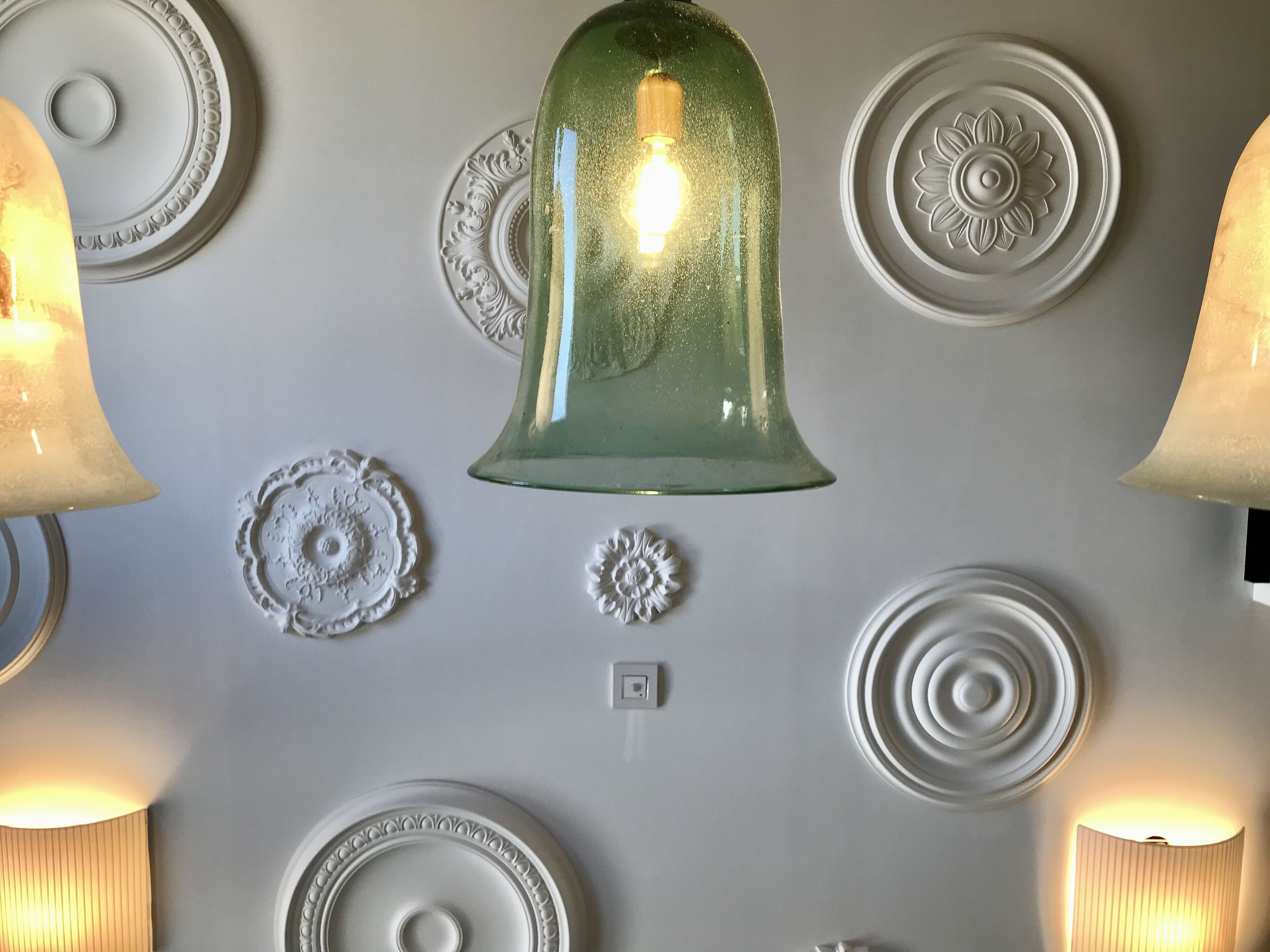 A wall with decorative plates and a green glass bell-shaped light fixture.