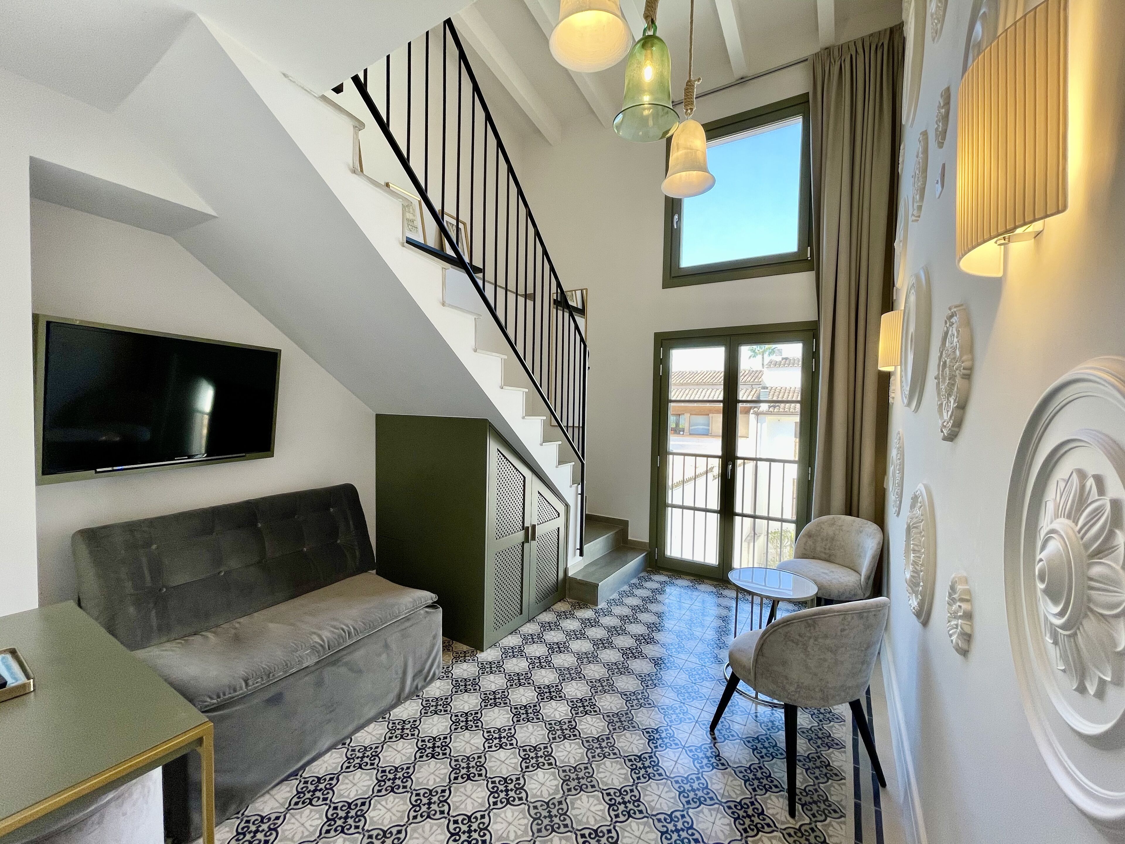 Un salon moderne avec un escalier, un téléviseur à écran plat, un canapé gris, des carreaux de sol à motifs et un mur décoratif.