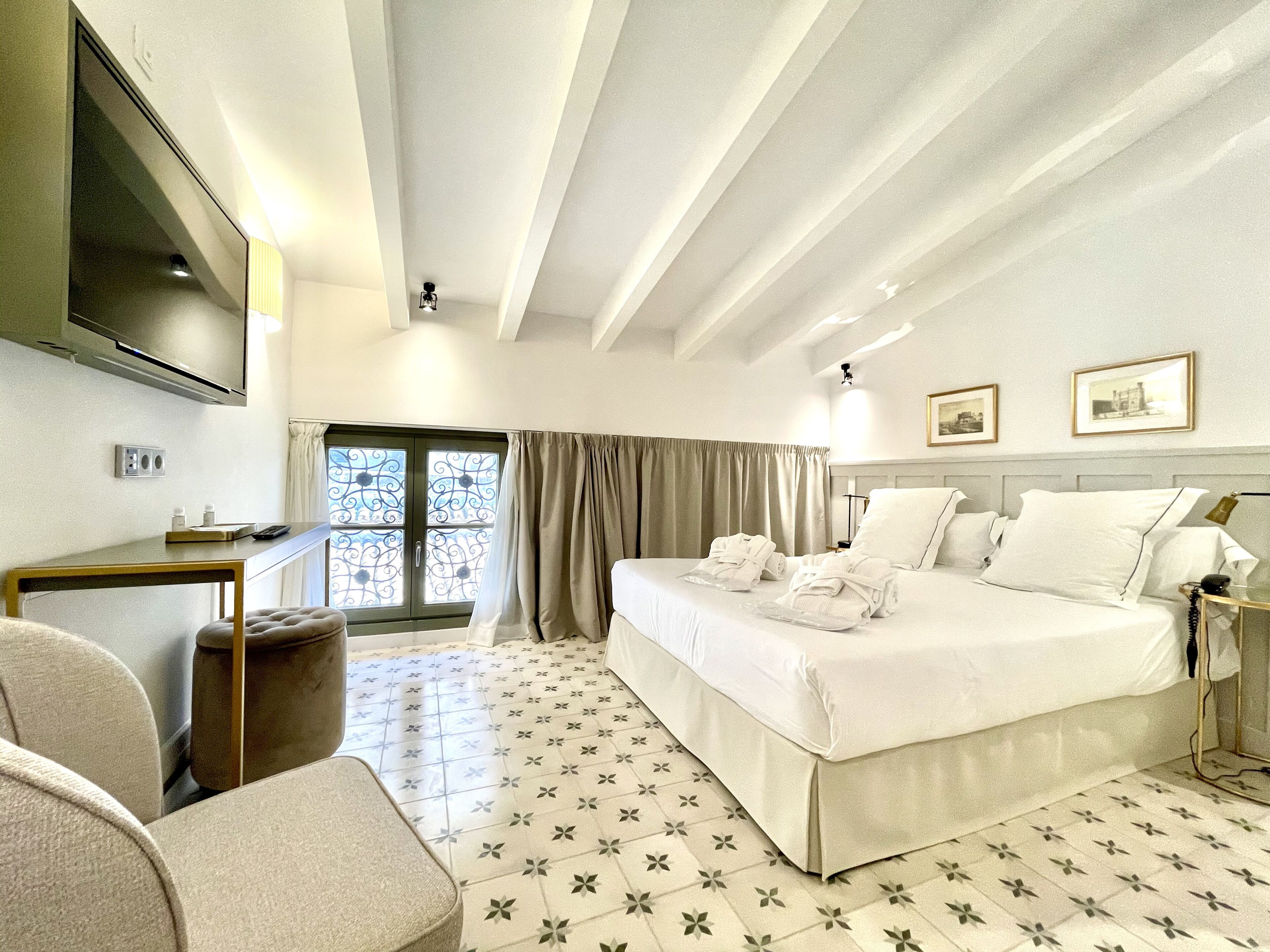 A hotel room with a bed, a desk, a chair, a TV, and a window with curtains.