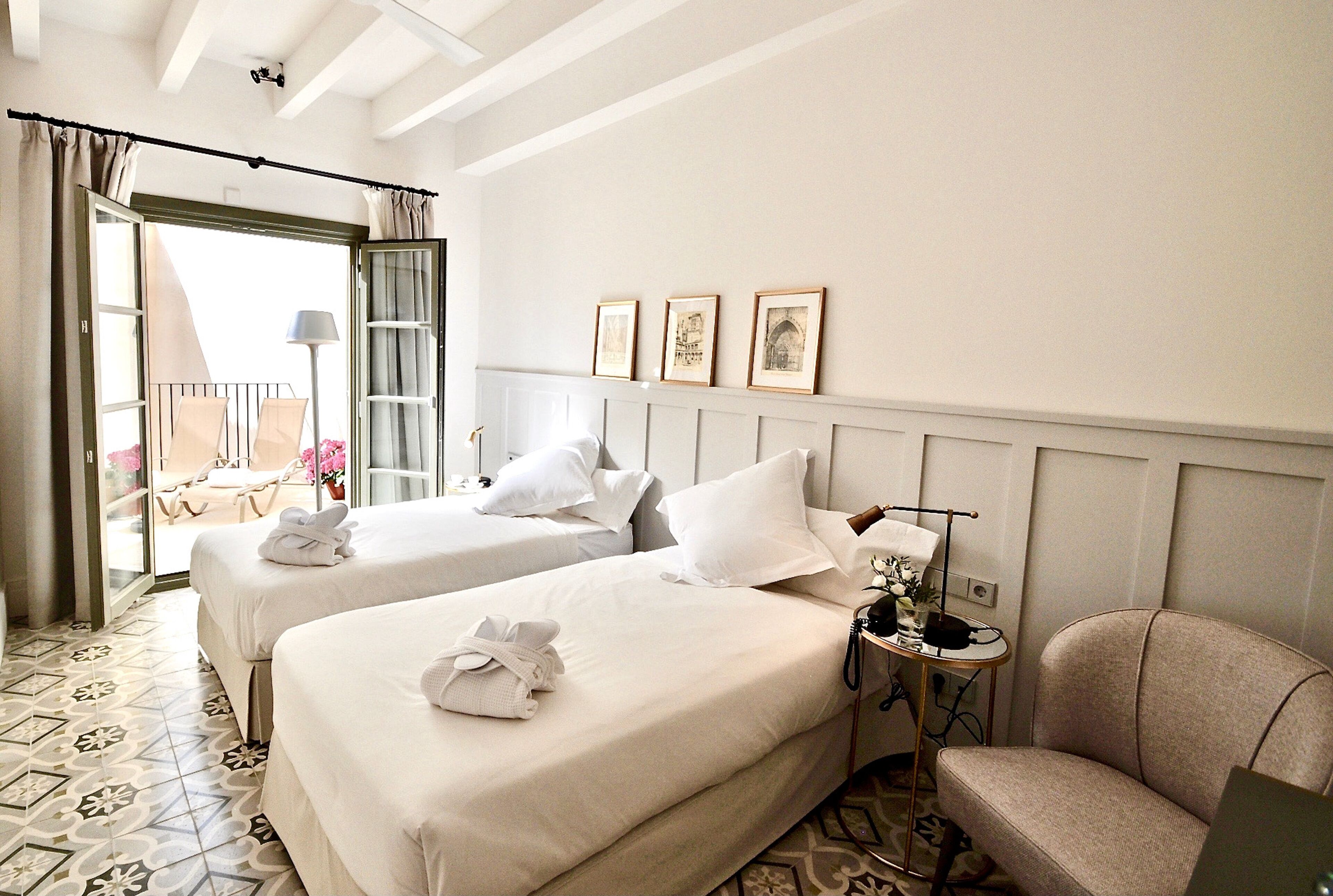 Ein Hotelzimmer mit zwei Betten, einem Sessel, einem kleinen Tisch und einem Balkon mit Sitzgelegenheit und Tisch.
