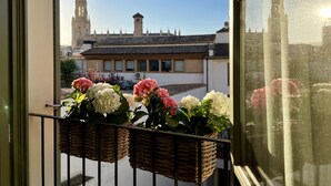 A balcony with wicker baskets containing flowers, overlooking a building with a tower and a tiled roof. - Hotel Basílica (Palma de Mallorca)