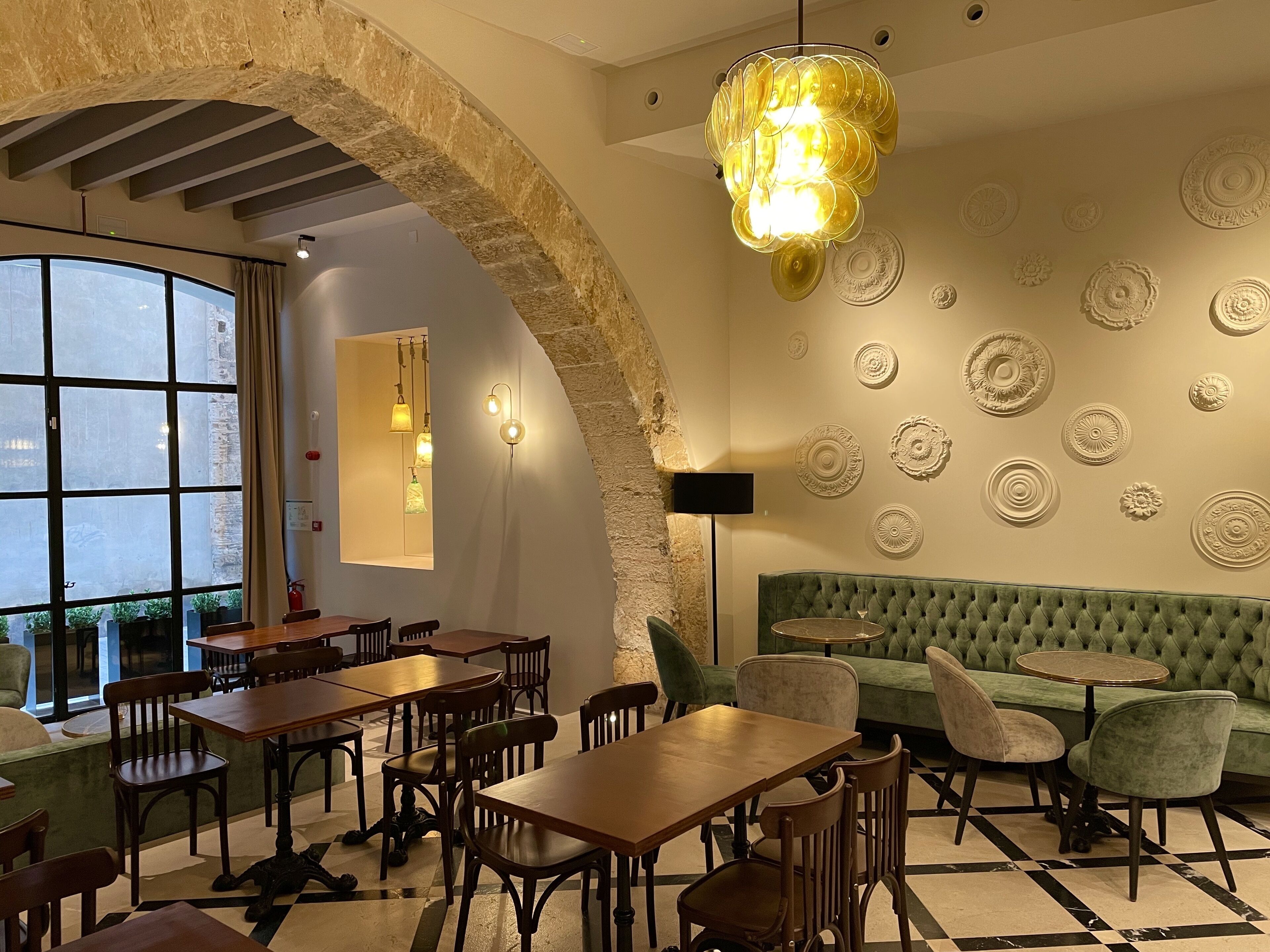 Un interior de restaurante con paredes de piedra, un banco acolchado verde, mesas de madera y una araña.