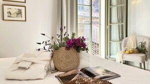 A neatly arranged bedroom with a bed, a woven basket with flowers, a book, and a chair with a hat. - Hotel Basílica (Palma de Mallorca)