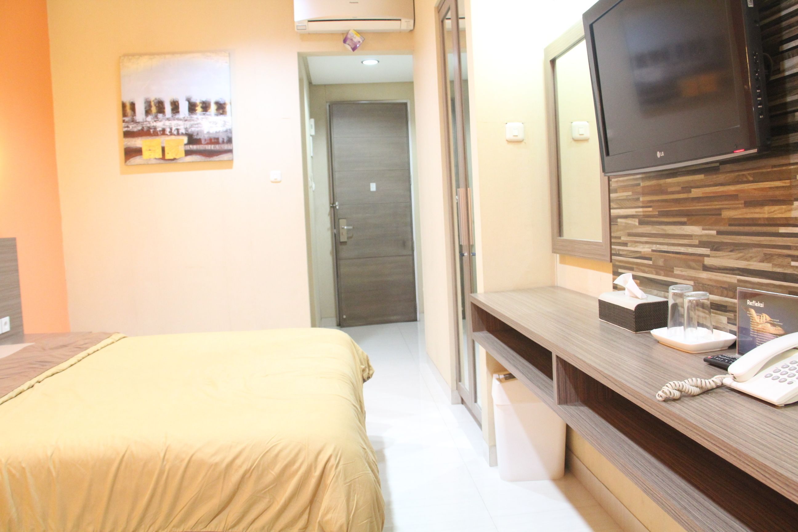 Habitación de hotel con cama, escritorio con teléfono, televisor y puerta que da a otra habitación.