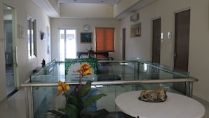 A reception area with a glass partition, a clock, a window with blinds, and a small table with a sculpture. - Tirta Mansion Premier (Curug)