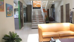 A modern lobby with a staircase, a reception desk, and a seating area with a sofa. - Tirta Mansion Premier (Curug)