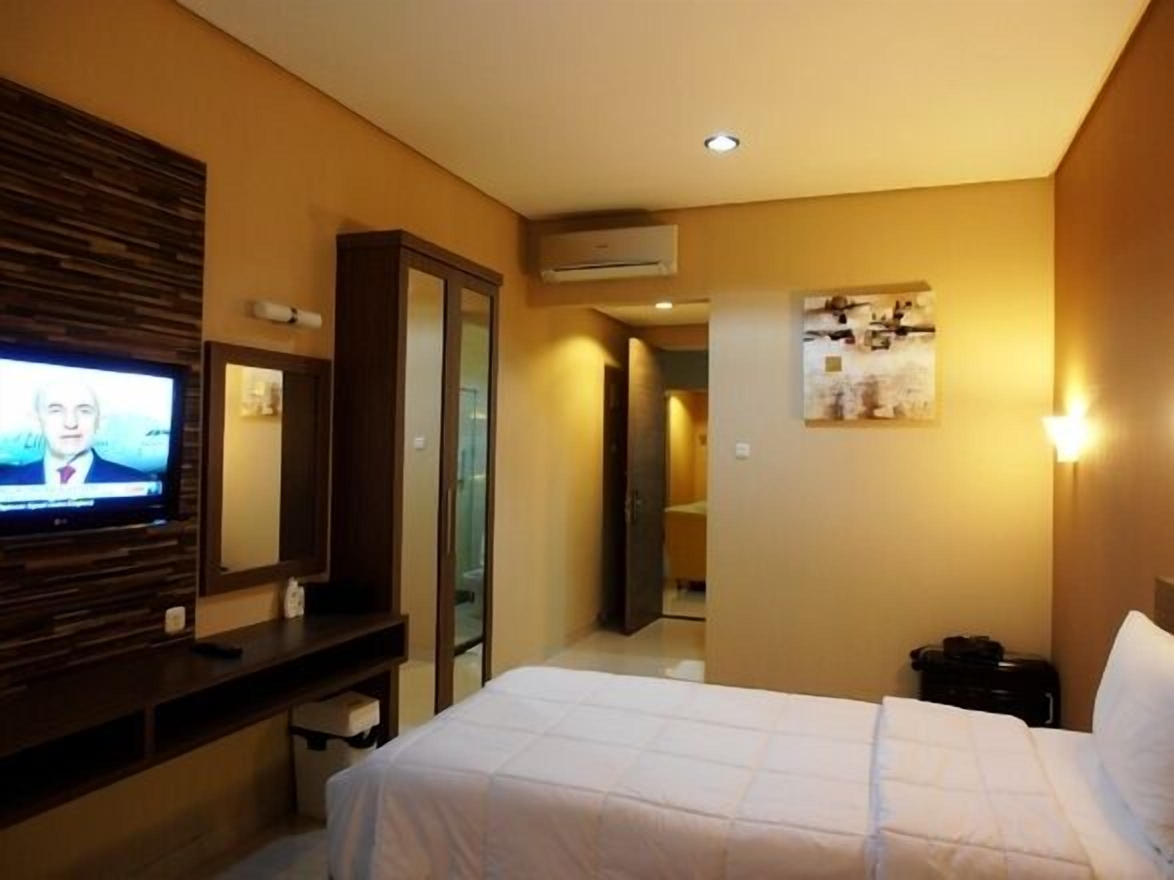 Quarto de hotel com cama, televisão na parede, secretária e espelho.