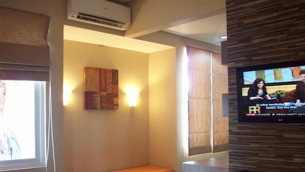A hotel room with a bed, a bench, a television mounted on the wall, and a window with blinds. - Tirta Mansion Premier (Curug)