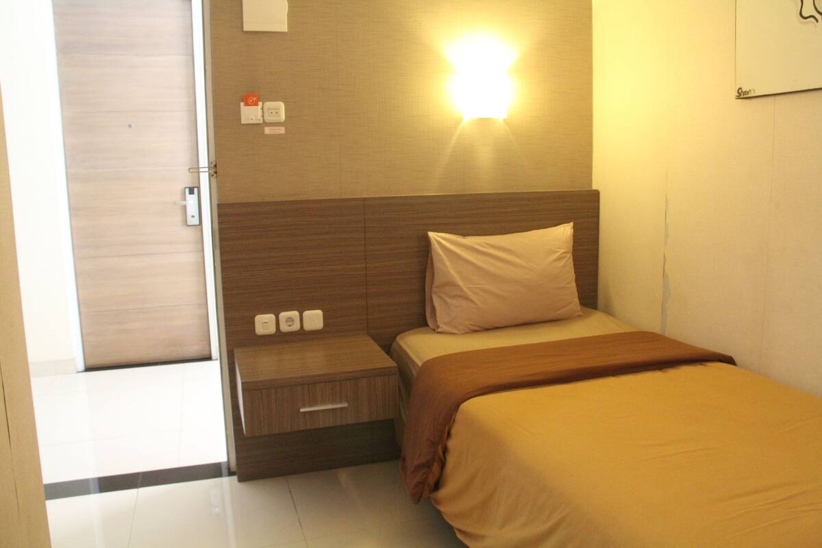 A hotel room with a bed, bedside table, and a wall-mounted light.