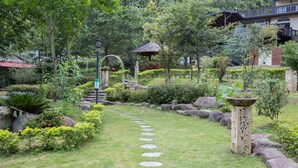 Un sendero en un jardín con piedras para pisar, rodeado de abundante vegetación y un quiosco tradicional.