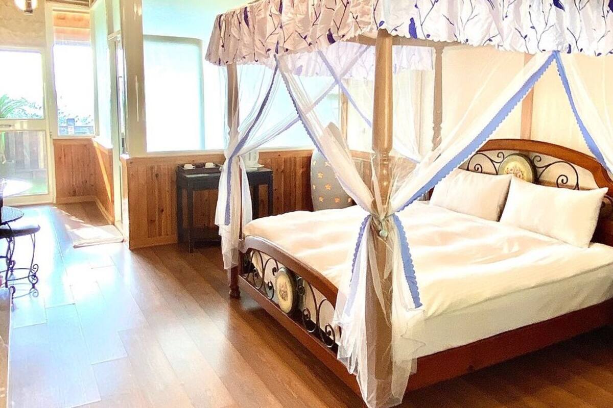 A bed with a canopy, wooden flooring, and a window with a view.