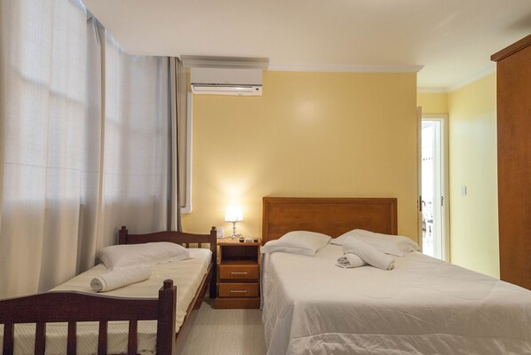 A hotel room with two single beds, a wooden nightstand with a lamp, and an air conditioning unit on the wall. - Apartamento Du Centre (Gramado)