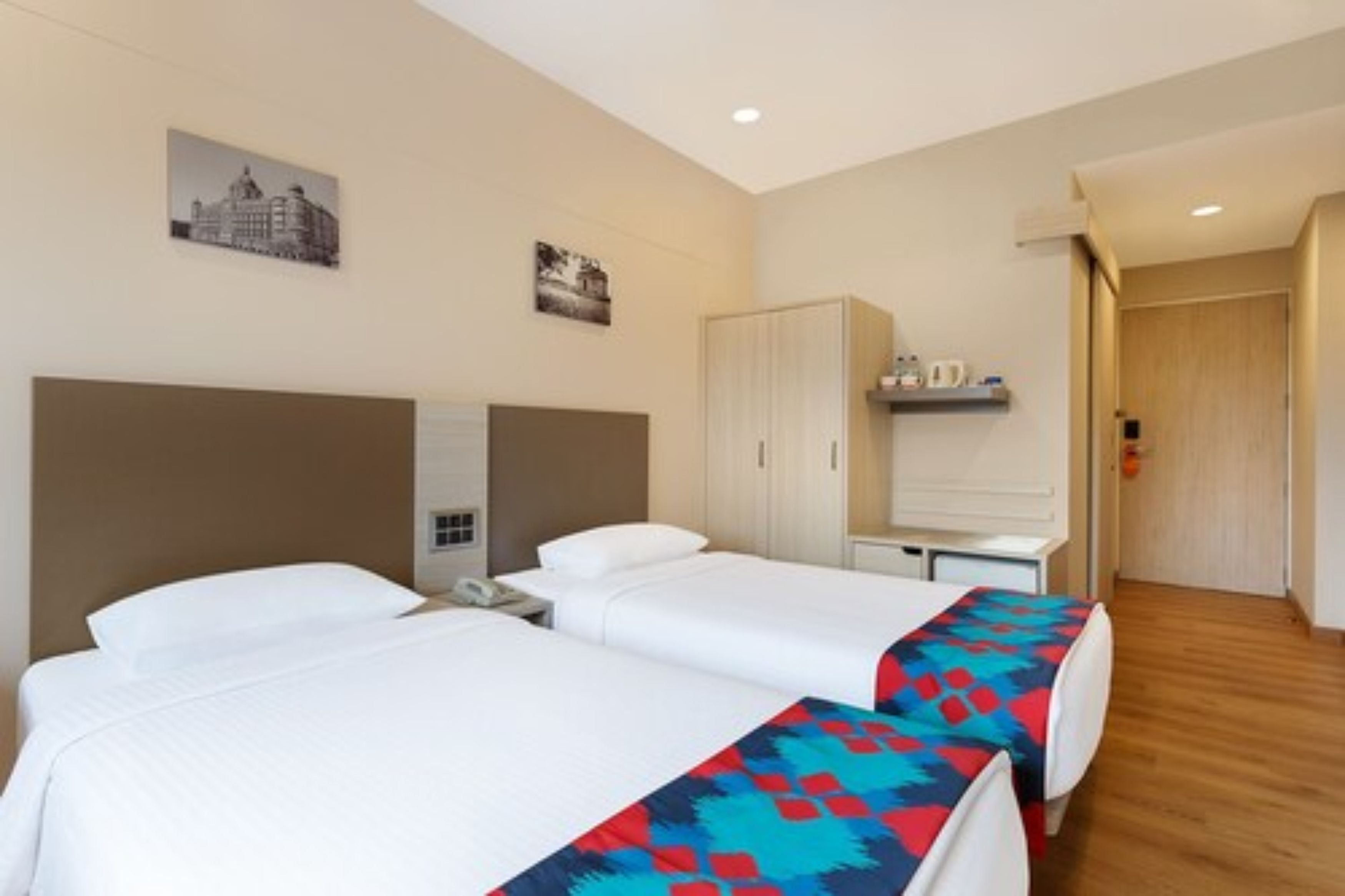 Habitación de hotel con dos camas, un armario, un escritorio con silla y una mesita con lámpara.