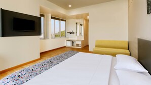 A modern hotel room with a large bed, a flat-screen TV mounted on the wall, a yellow armchair, and a small desk with a mirror. - Ginger Aurangabad (Chhatrapati Sambhajinagar)