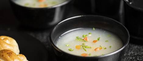 Tres tazones negros de sopa con vegetales, acompañados de un plato de pan.