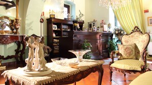 Una habitación con un armario de madera, un sillón floral, una mesa con un centro de mesa decorativo y una araña.