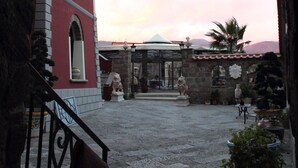 Un arco que da a un patio con un edificio rojo, estatuas de piedra y plantas en macetas.
