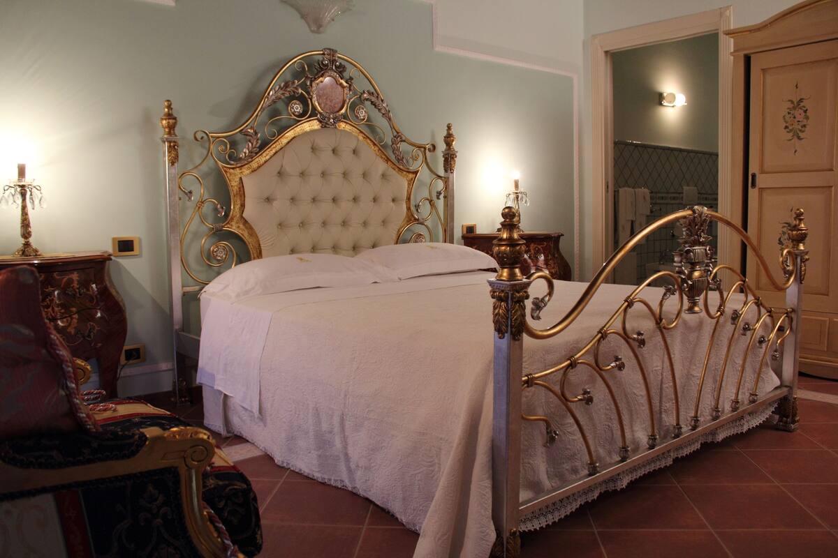 Un dormitorio con una cama de dos columnas de estilo clásico, un armario de madera y una mesita con una lámpara.