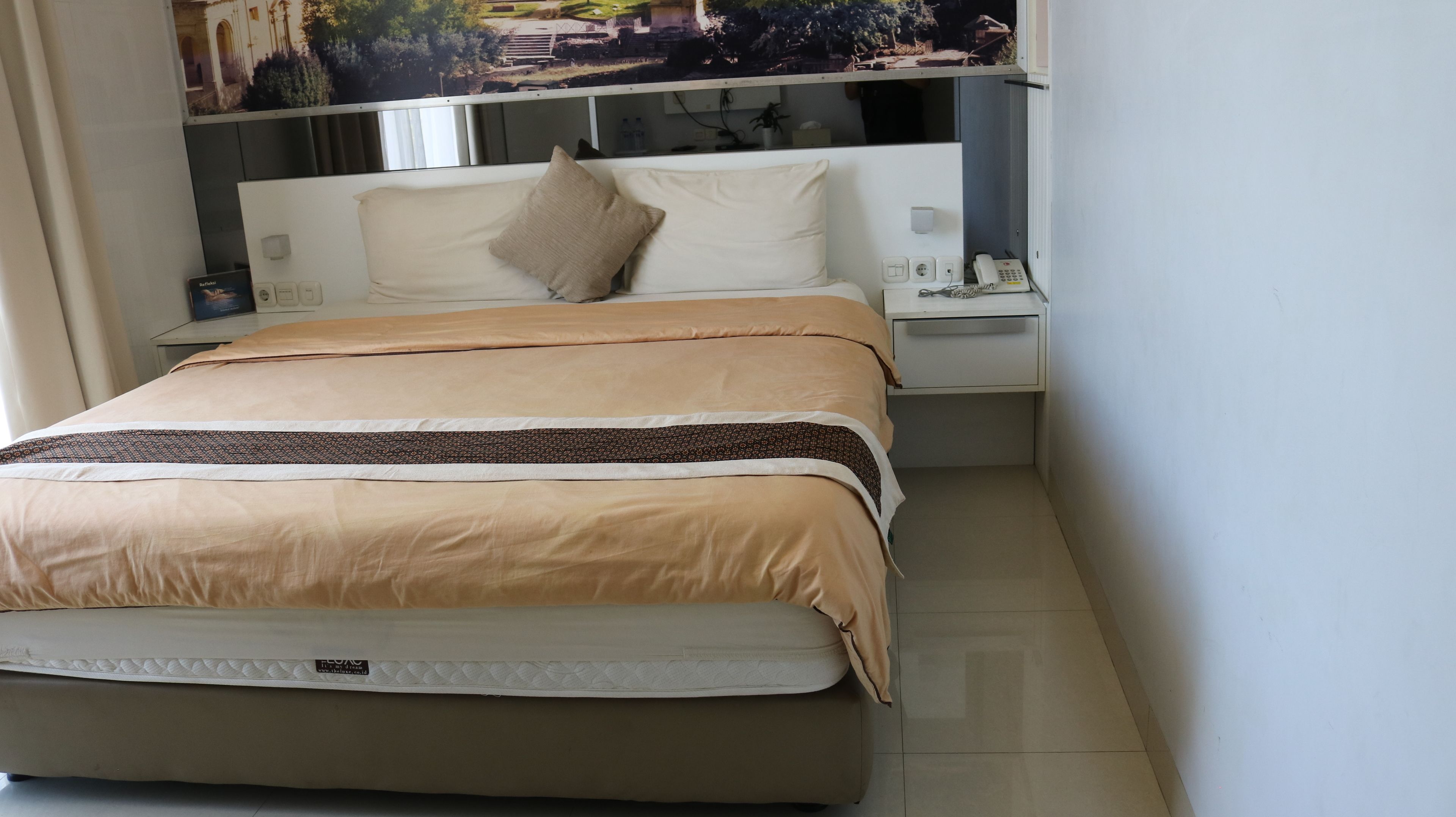 A neatly made bed with a beige and brown bedspread, a white pillow, and a headboard with a built-in telephone.